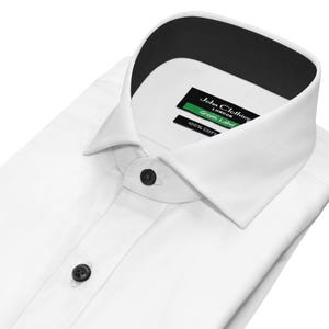 May include: A crisp white dress shirt with a black collar lining and black buttons. The shirt has a classic collar style and is folded neatly. A green and black label reads "John Clothier London Green Label" and "100% COTTON".