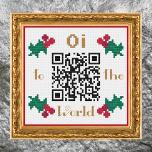 May include: A white cross-stitch pattern with a black and white QR code in the center. The text "Oi to the World" is written in gold lettering above and below the QR code. The pattern is surrounded by green holly leaves with red berries.