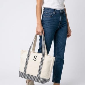 Puede incluir: Bolso tote de lona color crema con detalles de cuadros vichy en blanco y negro. La bolsa presenta una letra "S" negra en la parte delantera. Las asas y el borde inferior son de tela de cuadros vichy. Un accesorio elegante y pr&aacute;ctico.