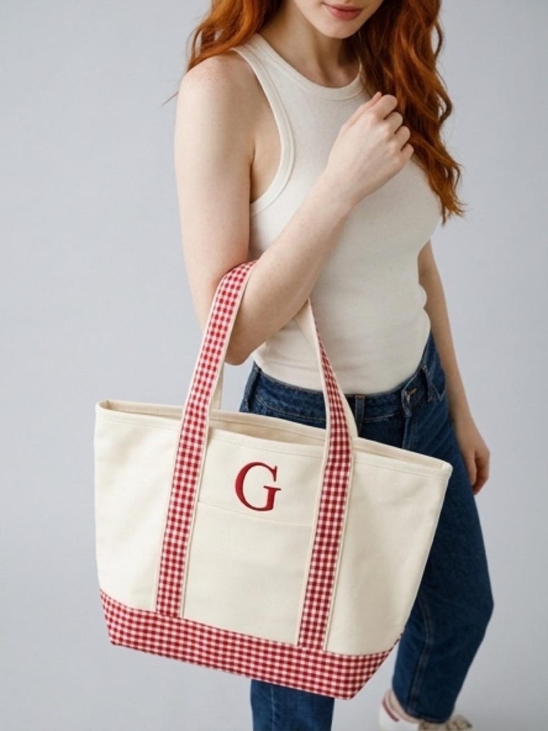 Puede incluir: Bolso tote de lona color crema con ribete y asas de cuadros rojos. Presenta la letra "G" bordada en rojo en el bolsillo delantero. Un accesorio elegante y pr&aacute;ctico.