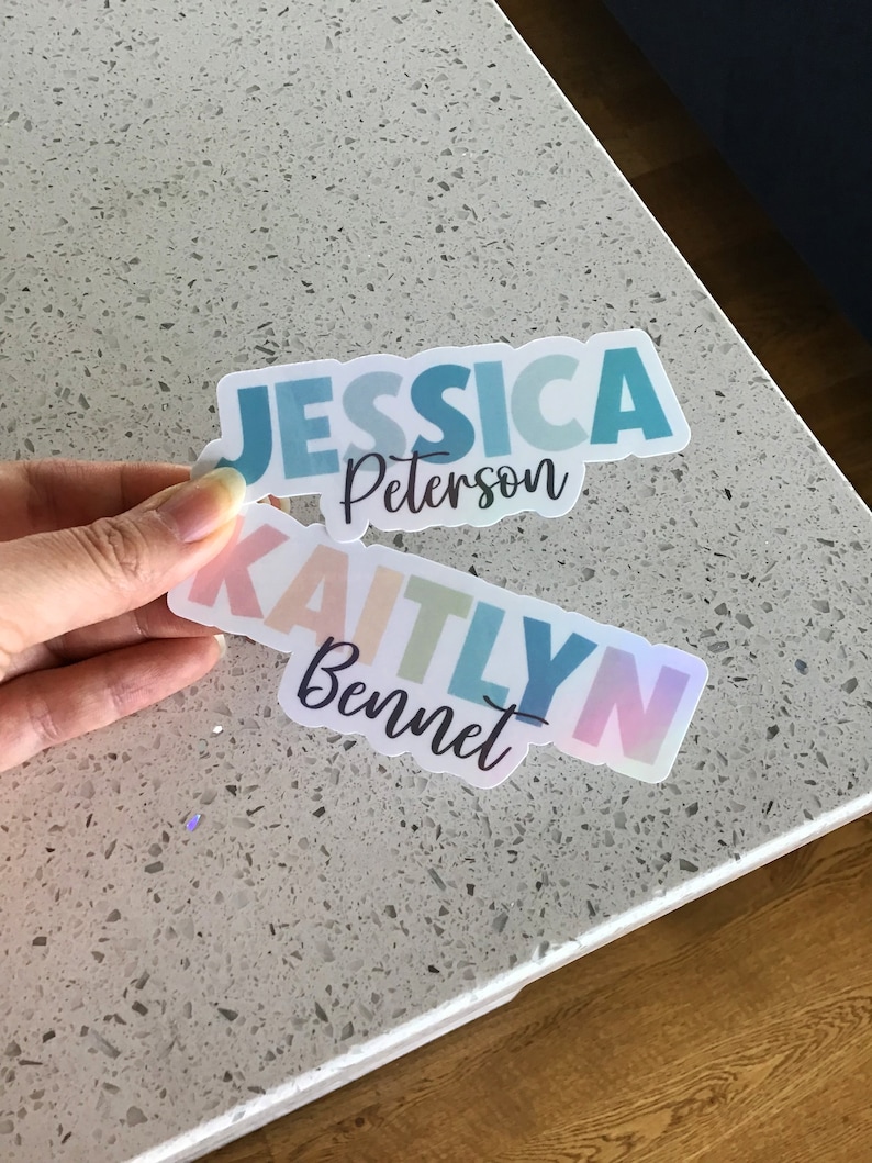 May include: Two colorful stickers with names on them. The top sticker is blue and says "Jessica Peterson". The bottom sticker is rainbow colored and says "Kaitlyn Bennet".