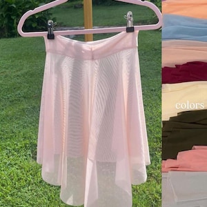 Op de afbeelding: Een lichtroze balletsrok van doorschijnende stof, hangend aan een roze hanger. De rok heeft een gelaagd ontwerp en een zachte, vloeiende uitstraling. Een kleurenkaart met stofstalen is rechts zichtbaar.