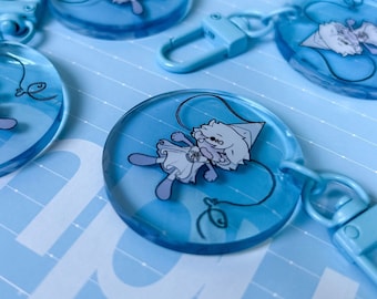 May include: A set of blue keychains with a cartoon character design. Each keychain features a different character with a white outline and a blue background. The keychains are made of clear plastic and have a metal ring for attaching keys.