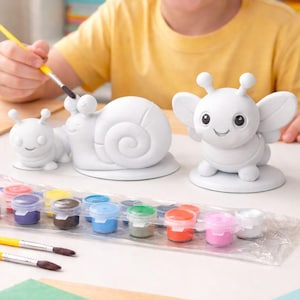 May include: A child paints a white ceramic snail and a butterfly figurine with a set of colorful paints. The paint set includes various colors, and the child is using a paintbrush. The scene is set on a white table.