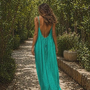 Puede incluir: Un vestido largo de color azul cerceta vibrante que presenta un diseño de espalda abierta profunda con tirantes finos y una silueta fluida y fruncida que llega hasta los tobillos, mostrando una textura de tela sólida y sin estampados.
