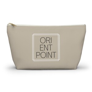 May include: A beige zippered pouch with a white border around the text "ORIENT POINT" in black.