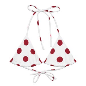 May include: White bikini top with a red polka dot pattern. The triangle-shaped top has tie closures at the neck and back. The red polka dots are evenly spaced across the white fabric. This swimwear is perfect for a summer day at the beach or pool.