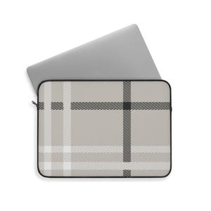 May include: A laptop sleeve with a beige plaid pattern, featuring black and white stripes. The sleeve has a black zipper and a black border. A silver laptop is partially inserted into the sleeve.