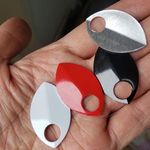 May include: Four leaf-shaped scales with a single circular hole at the base. The set includes one silver-toned metallic scale, one glossy black scale, one vibrant red scale, and one smooth white scale, all featuring a pointed tip.