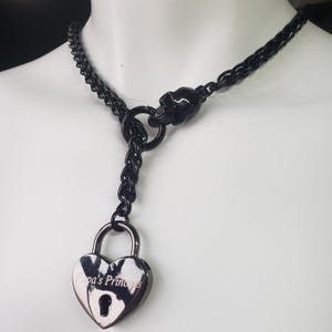 Puede incluir: Collar gargantilla de metal negro con cierre de calavera y un candado en forma de corazón con la inscripción "Papa's Princess".