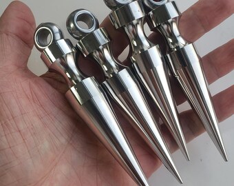 Puede incluir: Cuatro puntas de metal plateado pulido, cada una con un cuerpo cónico y un ojal circular en la parte superior. Estos componentes metálicos tienen un acabado liso y reflectante y están dispuestos en una fila paralela, mostrando sus puntas.