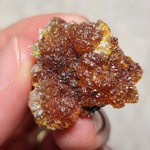 Puede incluir: Primer plano de un pequeño cristal de forma irregular, marrón y amarillo. El cristal tiene una superficie rugosa y texturizada y parece ser translúcido.