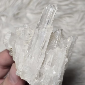 Puede incluir: Un grupo de cristales de cuarzo transparentes. Los cristales son de color blanco translúcido y están agrupados, creando una apariencia texturizada y natural. Los cristales son de diferentes tamaños y formas.