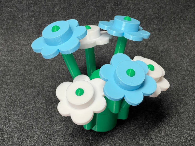 Puede incluir: Un ramo de flores estilizadas en un jarr&oacute;n. Las flores tienen p&eacute;talos azul claro y blancos con centros y tallos verdes. El jarr&oacute;n y los tallos son verdes. Las flores est&aacute;n dispuestas en un grupo.