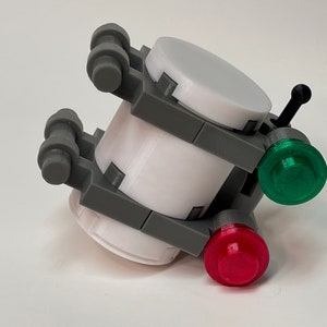 May include: A 3D-printed model featuring a cylindrical white body with gray structural supports. It has two colored lights, one red and one green, and a small black antenna. The model is designed with a futuristic aesthetic.