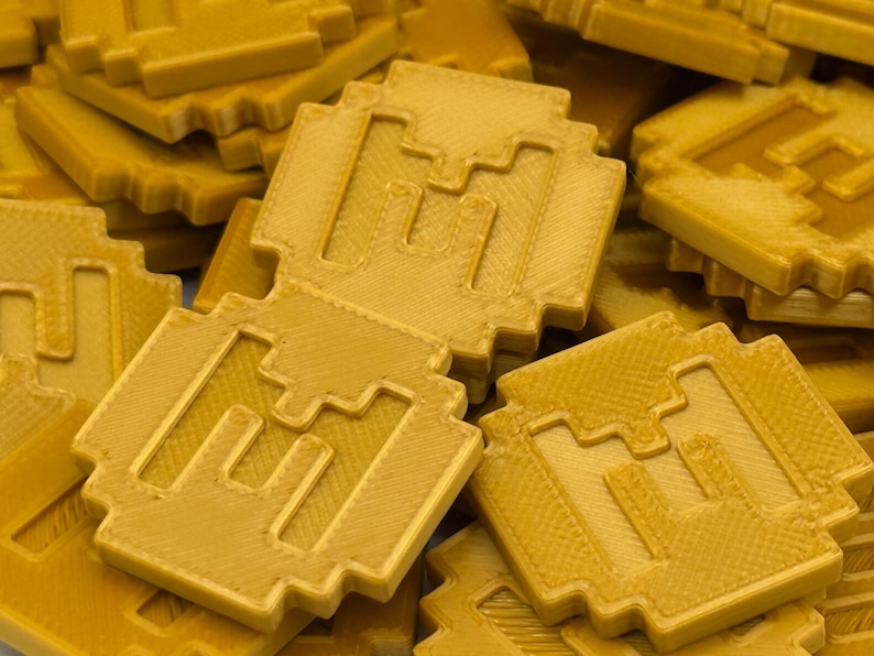May include: A pile of gold-colored, pixelated coins. Each coin has a square shape with a stylized letter "M" in the center. The coins have a textured surface and a slightly rounded edge, giving them a three-dimensional appearance.