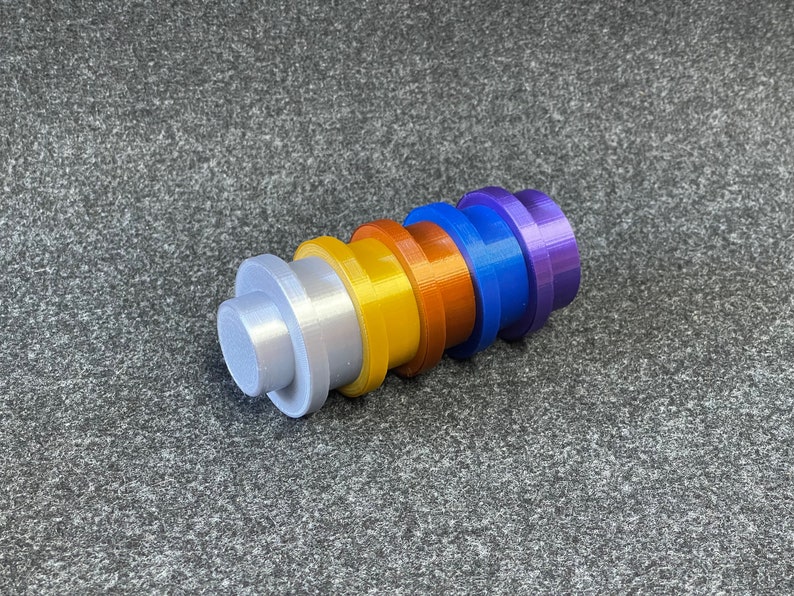 May include: A collection of six colorful, cylindrical objects in a row. The colors include silver, yellow, orange, blue, and purple. Each object has a flat, circular base and a smaller, raised cylinder on top.