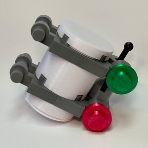 May include: A 3D-printed model featuring white cylindrical components, gray structural supports, and a black antenna. It has a green and a red button. The model is designed with a futuristic aesthetic.