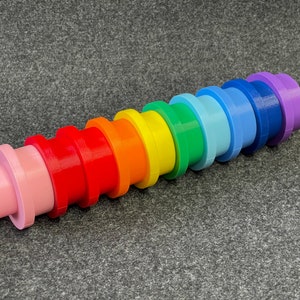 May include: A colorful, rainbow-colored toy made of plastic. The toy is composed of stacked, cylindrical pieces in a spectrum of colors, including pink, red, orange, yellow, green, blue, and purple. The toy is designed for stacking and building.