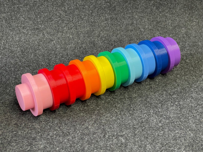 May include: A colorful, rainbow-colored toy made of plastic. The toy is composed of stacked, cylindrical pieces in a spectrum of colors, including pink, red, orange, yellow, green, blue, and purple. The toy is designed for stacking and building.