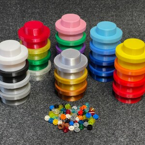 May include: A collection of colorful, 3D-printed building block accessories. Stacks of various colors, including red, pink, blue, and yellow, are arranged around a pile of small, translucent pieces. The pieces are designed to fit together.