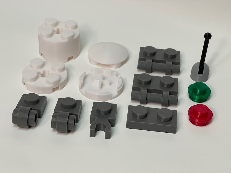 May include: Assorted plastic building block pieces in white, gray, green, and red. Includes various shapes like cylinders, plates, and connectors. A black antenna-like piece is also present. Ideal for creative construction.
