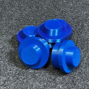 May include: A cluster of bright blue, 3D-printed components. Each has a circular base and a smaller, cylindrical top. They are arranged on a textured, grey surface. The components appear small, possibly parts for a larger assembly.