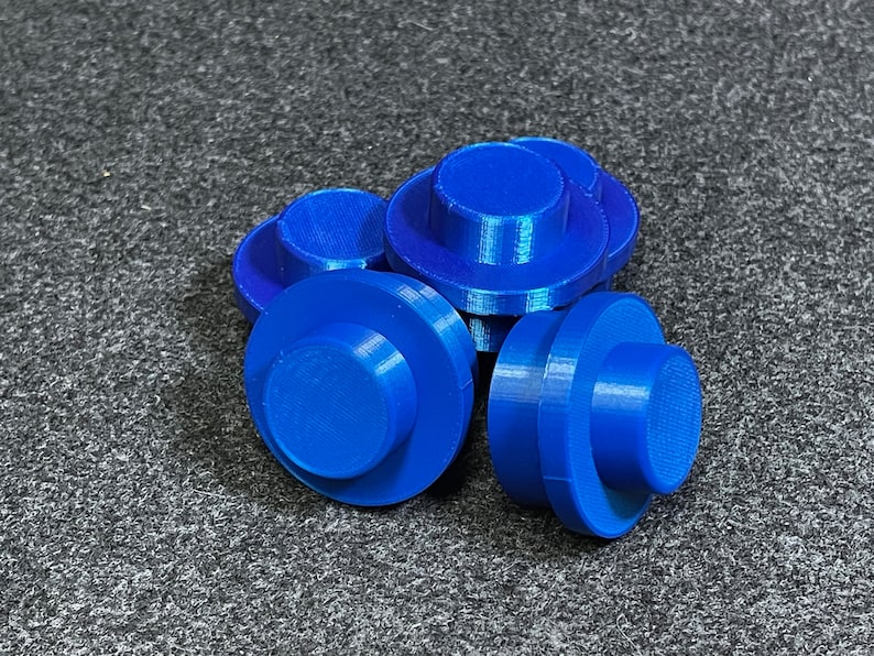 May include: A cluster of bright blue, 3D-printed components. Each has a circular base and a smaller, cylindrical top. They are arranged on a textured, grey surface. The components appear small, possibly parts for a larger assembly.