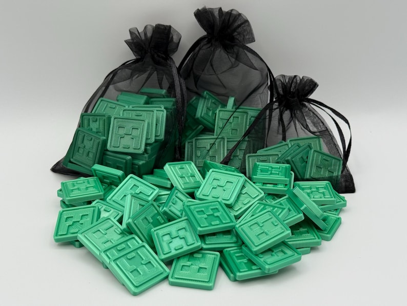 Puede incluir: Piezas de juego cuadradas verdes con una letra "M" estilizada esparcidas sobre una superficie blanca. Tres bolsas de malla negras llenas de las mismas piezas verdes est&aacute;n en el fondo. Las piezas son de color verde claro.