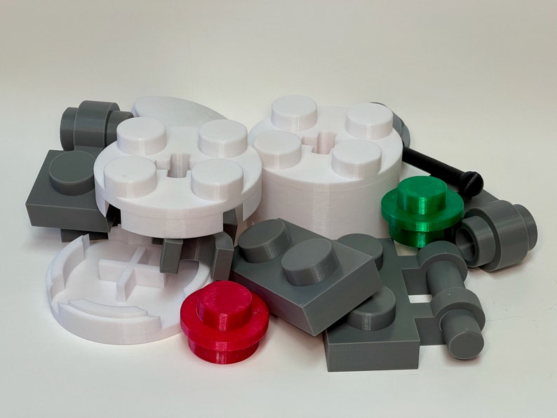 May include: A collection of various plastic building blocks in different shapes and colors. The blocks include gray, white, red, and green pieces, with a black screw. The pieces are designed to interlock.