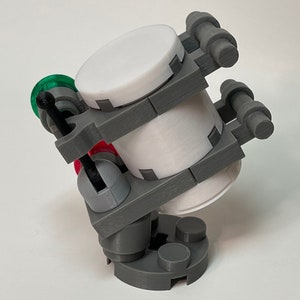 May include: A 3D-printed model of a futuristic device. The device features a cylindrical white container held within a gray frame. It has red and green accents, with a complex design and multiple cylindrical components.