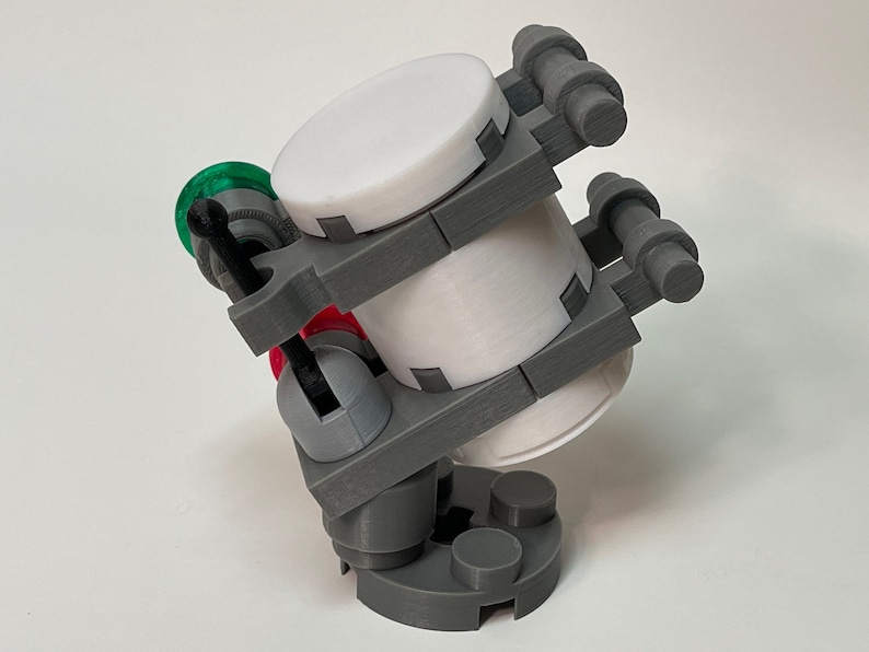 May include: A 3D-printed model of a futuristic device. The device features a cylindrical white container held within a gray frame. It has red and green accents, with a complex design and multiple cylindrical components.