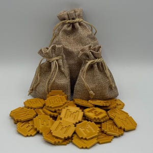 May include: Three burlap sacks with drawstring closures are arranged behind a pile of gold-colored game tokens. The tokens are square with a pixelated design. The sacks vary in size, with the largest in the center.