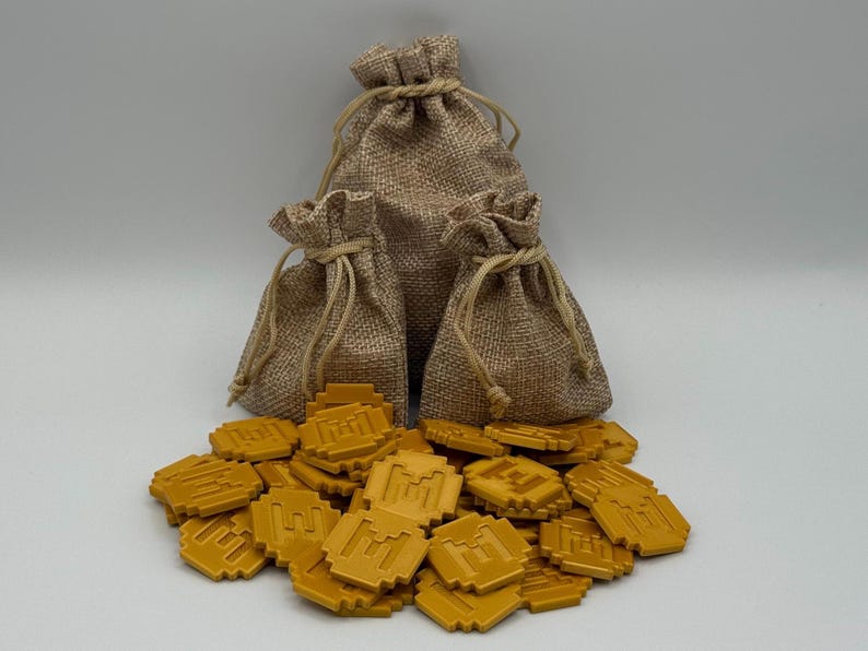 May include: Three burlap sacks with drawstring closures are arranged behind a pile of gold-colored game tokens. The tokens are square with a pixelated design. The sacks vary in size, with the largest in the center.