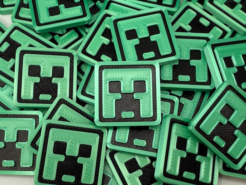 May include: A collection of square, green and black Minecraft-themed badges. Each badge features a pixelated face design with a green border. The badges are scattered across a surface, creating a textured pattern.
