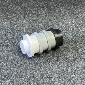May include: A multi-colored bottle stopper with a stepped design. The stopper is composed of white, light gray, dark gray, and black sections. The object is cylindrical and appears to be made of plastic.