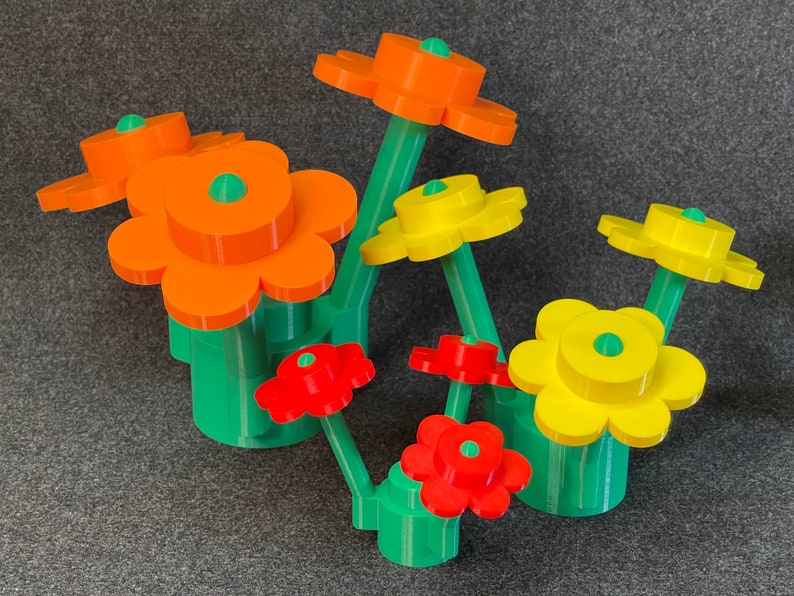 Puede incluir: Un grupo de flores coloridas y estilizadas en naranja, amarillo y rojo, con tallos y bases verdes. Las flores tienen un dise&ntilde;o de p&eacute;talos en capas y un centro verde. El arreglo est&aacute; sobre un fondo gris.