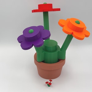 Puede incluir: Un arreglo floral caprichoso en una maceta de terracota. Las flores son rojas, naranjas y moradas con tallos y centros verdes. Un peque&ntilde;o grupo de flores rojas se encuentra en la base.