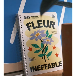 Könnte beinhalten: Ein gelbes Notizbuch mit einem floralen Design und dem Text "FLEUR INEFFABLE" auf dem Cover. Die Blumen sind blau, grün und orange. Der Text "GET UP ASS SOONER WE GOT BIG SHIT TO DO TODAY" befindet sich ebenfalls auf dem Cover.