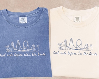 May include: Two t-shirts, one blue and one ivory, with a roller coaster graphic and the text "last ride before she's the bride" and "last ride before I'm the bride". The shirts are made of soft material.