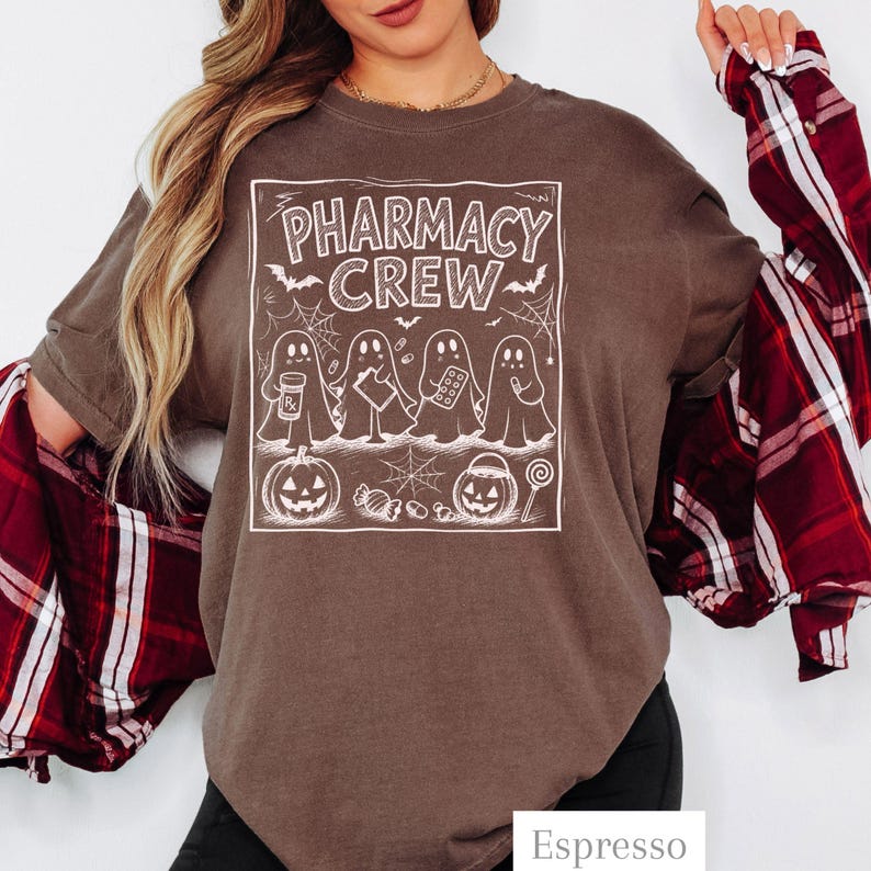 K&ouml;nnte beinhalten: Ein dunkelbraunes T-Shirt mit einem wei&szlig;en Grafikdruck und dem Text PHARMACY CREW. Das Design zeigt vier Geister, zwei K&uuml;rbisse, Spinnweben, Flederm&auml;use und verschiedene S&uuml;&szlig;igkeiten. Das T-Shirt wird &uuml;ber einem rot-schwarz karierten Flanellhemd getragen.
