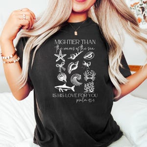 May include: Black t-shirt with white graphic of various sea creatures and the text "Mightier than the waves of the sea. Is His love for you. Psalm 93:4". The design includes a starfish, shells, and a crab.