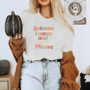 K&ouml;nnte beinhalten: Ein wei&szlig;es T-Shirt mit dem Text "Autumn leaves and cats please" in bunten, Retro-Lettern.