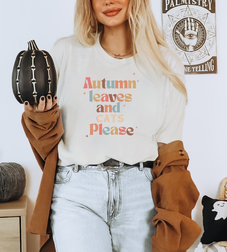 K&ouml;nnte beinhalten: Ein wei&szlig;es T-Shirt mit dem Text "Autumn leaves and cats please" in bunten, Retro-Lettern.