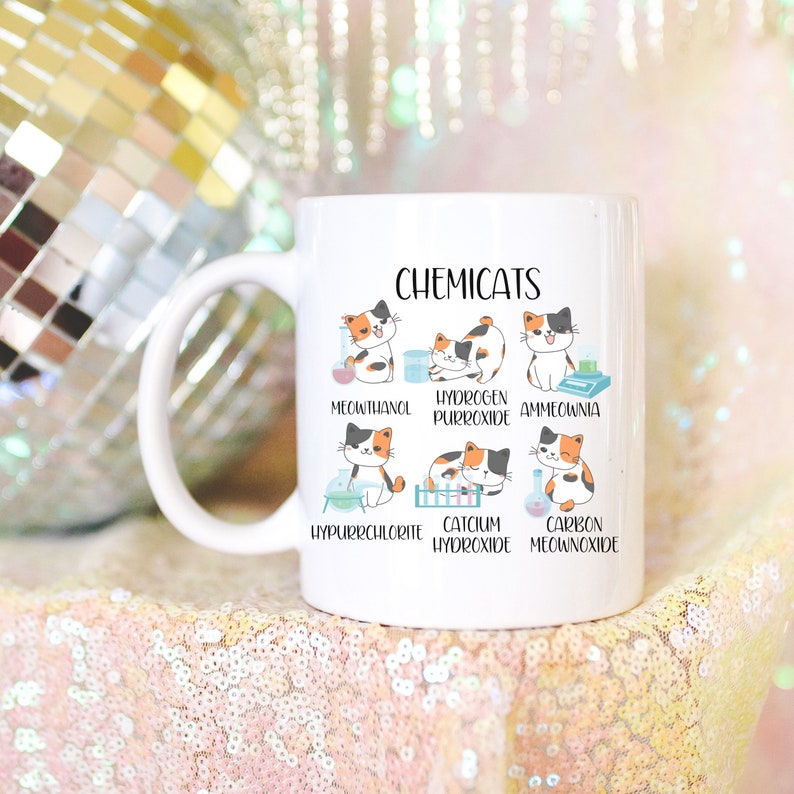 K&ouml;nnte beinhalten: Eine wei&szlig;e Keramiktasse mit einer Schwarzwei&szlig;illustration von Katzen mit chemischen Formeln. Der Text "Chemicats" befindet sich oben auf der Tasse. Die Katzenillustrationen sind mit katzenbezogenen chemischen Namen wie "Meownthanol" und "Hydrogen Purroxide" beschriftet.