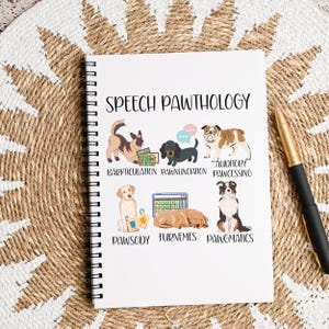 May include: White spiral-bound notebook with the title "SPEECH PAWTHOLOGY" and illustrations of various dog breeds. The notebook features humorous terms like "Barkticulation" and "Pawgnuniciation" related to dog communication. A gold and black pen rests on the right.