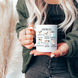 K&ouml;nnte beinhalten: Eine wei&szlig;e Keramiktasse mit einer humorvollen Illustration von Katzen, die verschiedene chemische Verbindungen darstellen. Der Text "Chemicats" ist oben auf der Tasse aufgedruckt. Die Katzenillustrationen sind mit den Namen der chemischen Verbindungen beschriftet, wie z. B. "Methanol", "Wasserstoffperoxid" und "Calciumhydroxid".