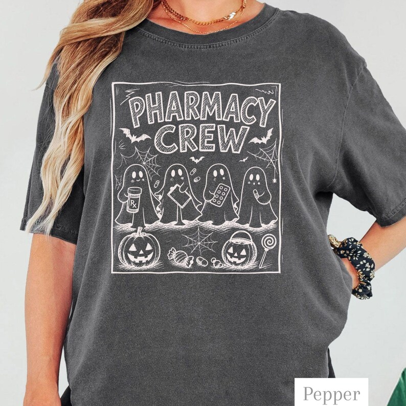 K&ouml;nnte beinhalten: Ein anthrazitfarbenes Kurzarm-T-Shirt mit einem wei&szlig;en Grafikdruck von vier Geistern, die Apothekenartikel halten. Der Text lautet PHARMACY CREW, erg&auml;nzt durch Illustrationen von Flederm&auml;usen, Spinnennetzen, zwei K&uuml;rbissen und verschiedenen S&uuml;&szlig;igkeiten.