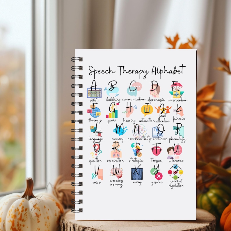 May include: A spiral-bound notebook titled "Speech Therapy Alphabet" featuring the alphabet with speech therapy terms and illustrations. The open notebook displays colourful, hand-drawn images and text, ideal for educational purposes. The notebook is on a wooden surface.