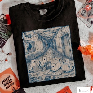 Puede incluir: Una camiseta negra con una ilustración gráfica en tonos azules de tres gatos fantasmales en un pasillo en ruinas. La escena incluye un letrero que dice ABA THERAPY, una caja marcada BEHAVIOR PLAN y un documento ABC DATA SHEET en el suelo.